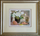 Framed artwork featuring white flowers in a vase, surrounded by fruit, including peaches and an olive jar, on a patterned cloth background.
