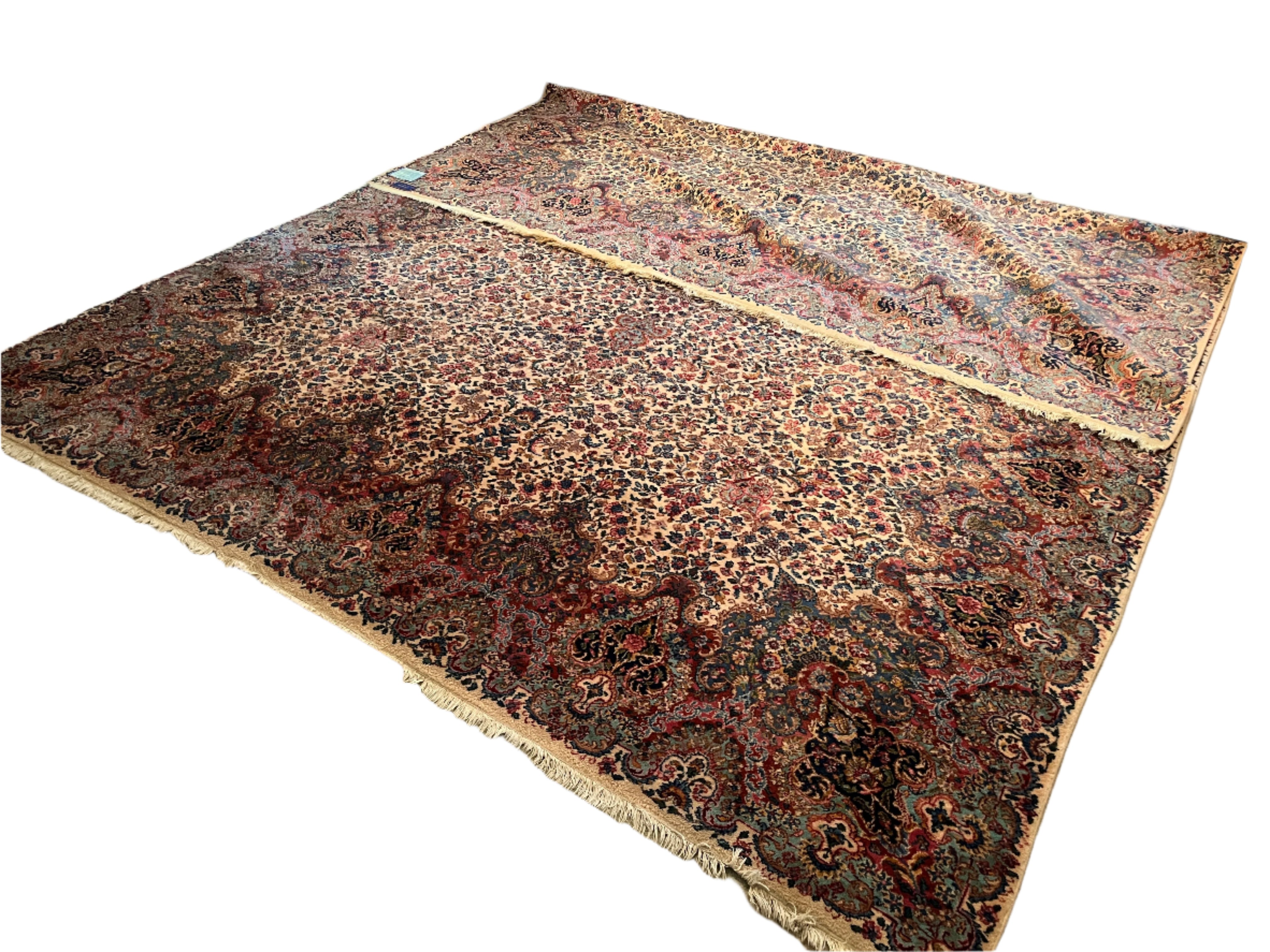 A large, intricately patterned rug covers a carpeted floor. There are two rugs overlapping, featuring rich colors and detailed designs. A sofa is visible.