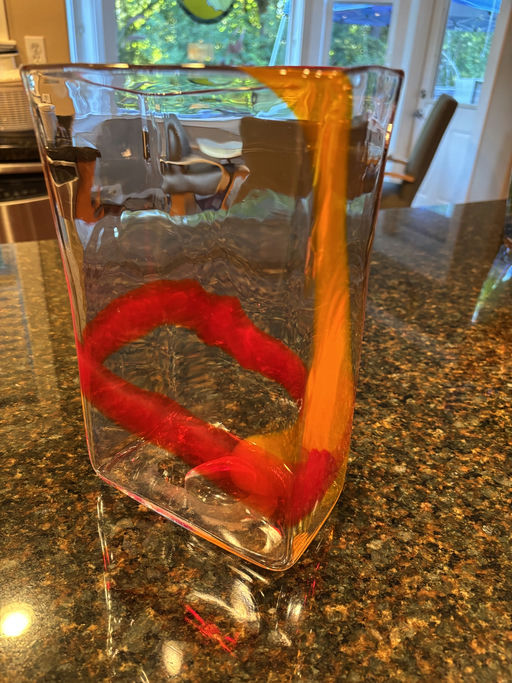 A clear pitcher filled with water shows vibrant orange and red ribbons swirling inside, reflecting colors on the glossy countertop.