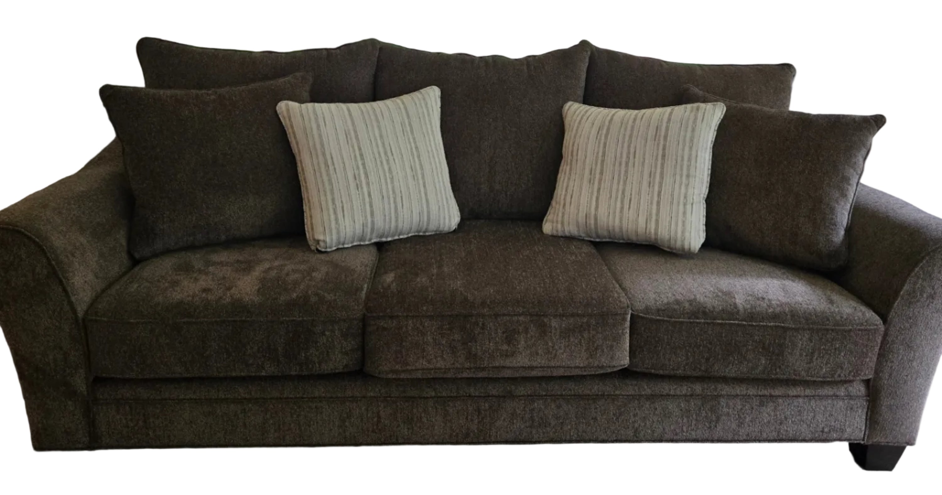 A cozy brown couch with two striped pillows sits in front of glass doors leading to a backyard, surrounded by trees and outdoor furniture.