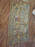 A decorative tapestry featuring a historical scene with horse riders, trees, and a distant cityscape, set on a wooden floor.