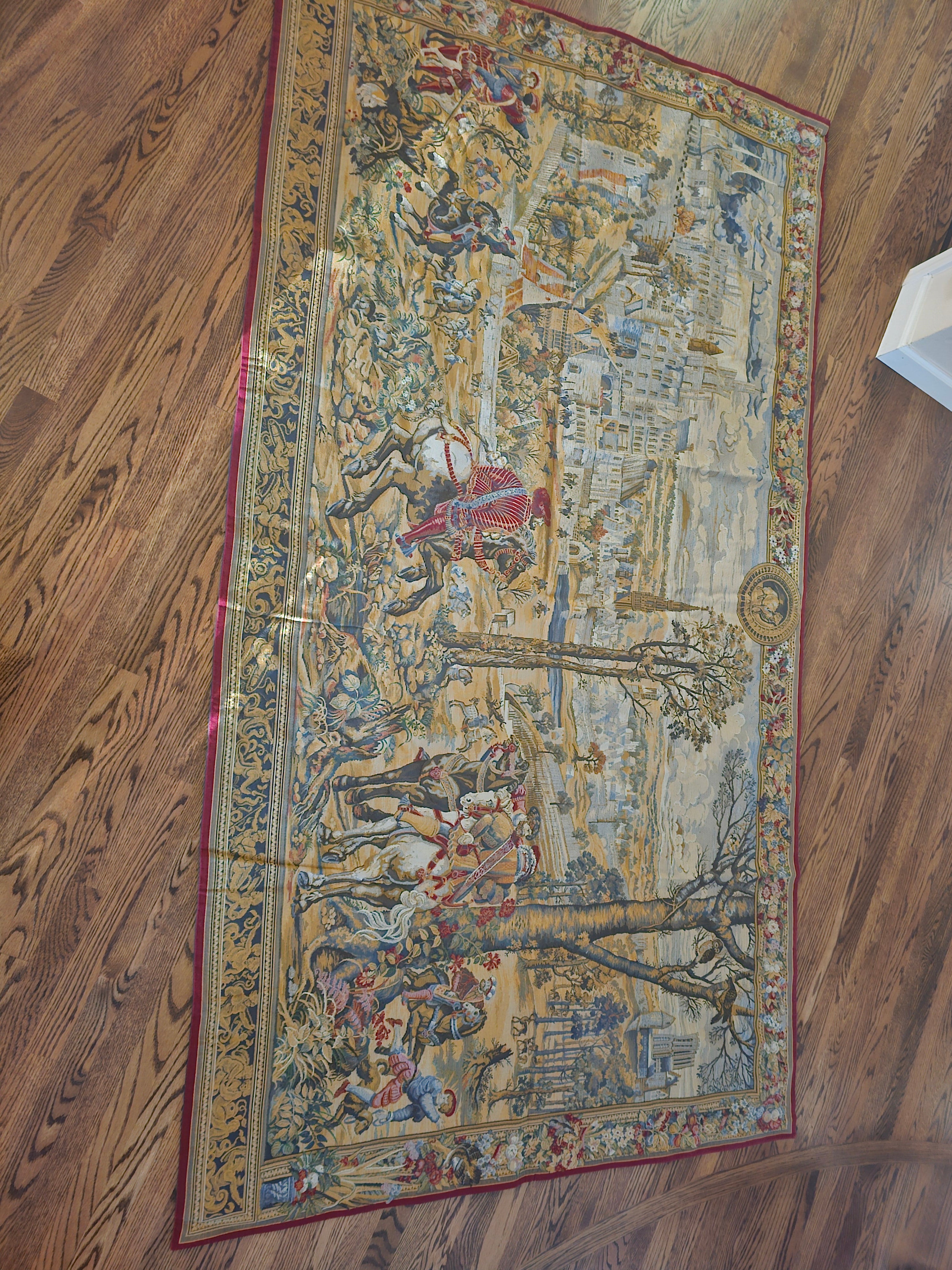 A decorative tapestry featuring a historical scene with horse riders, trees, and a distant cityscape, set on a wooden floor.