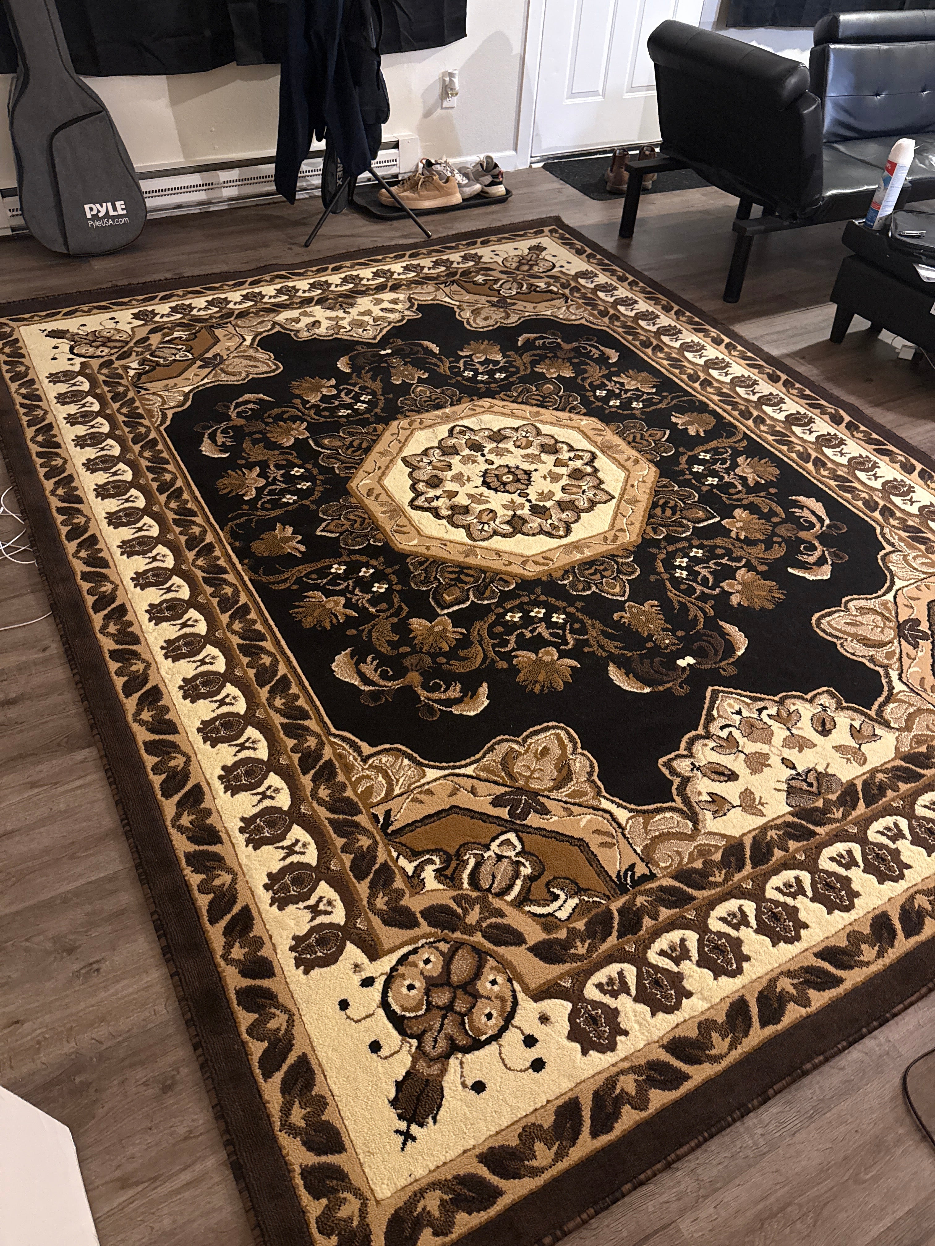 A detailed, ornate area rug with a floral pattern in shades of brown, cream, and gold, placed on a wood floor in a living space.