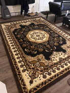 A detailed, ornate area rug with a floral pattern in shades of brown, cream, and gold, placed on a wood floor in a living space.