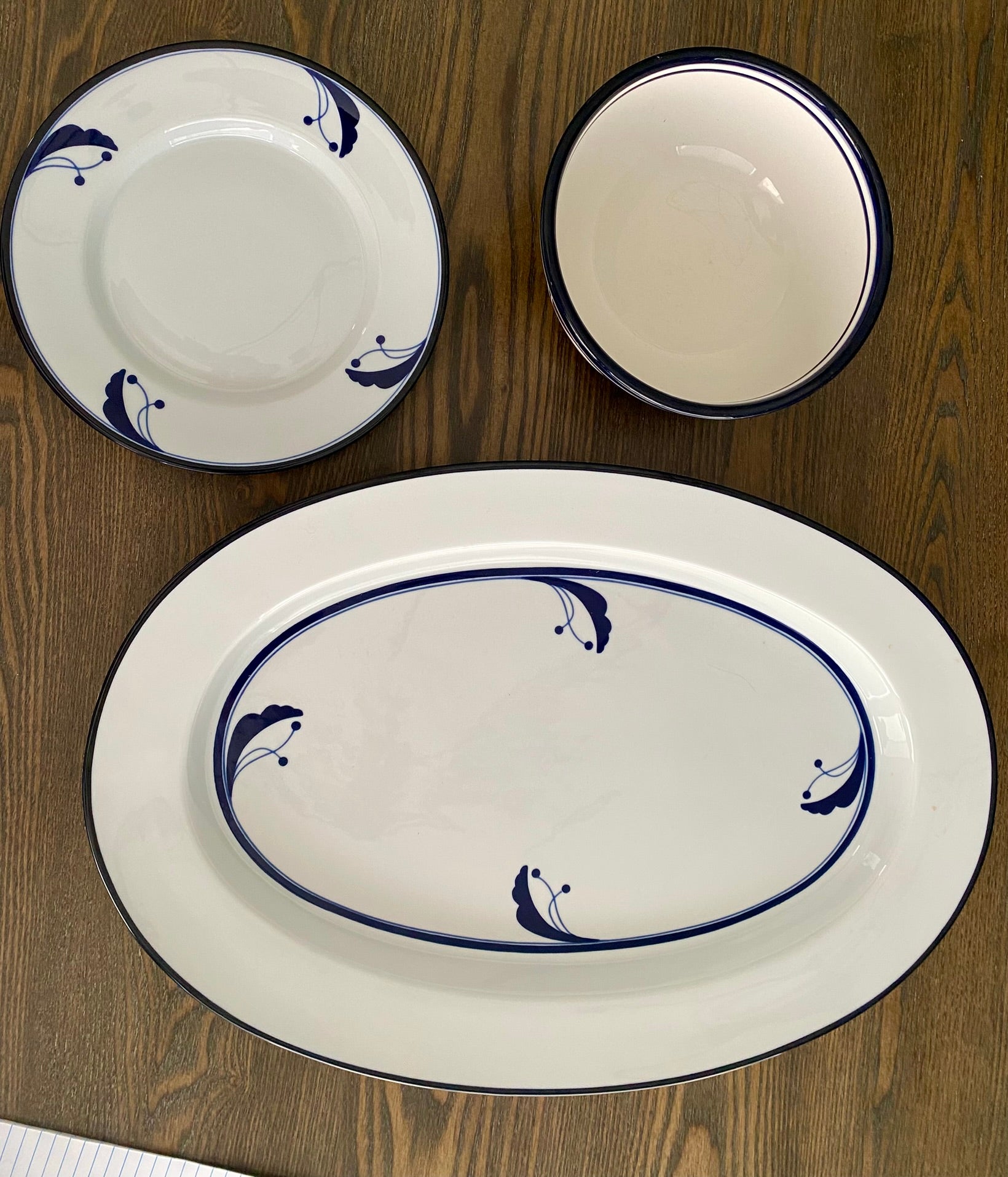 Three ceramic dishes arranged on a wooden table: one large oval platter and two smaller round dishes, all featuring a blue floral design.