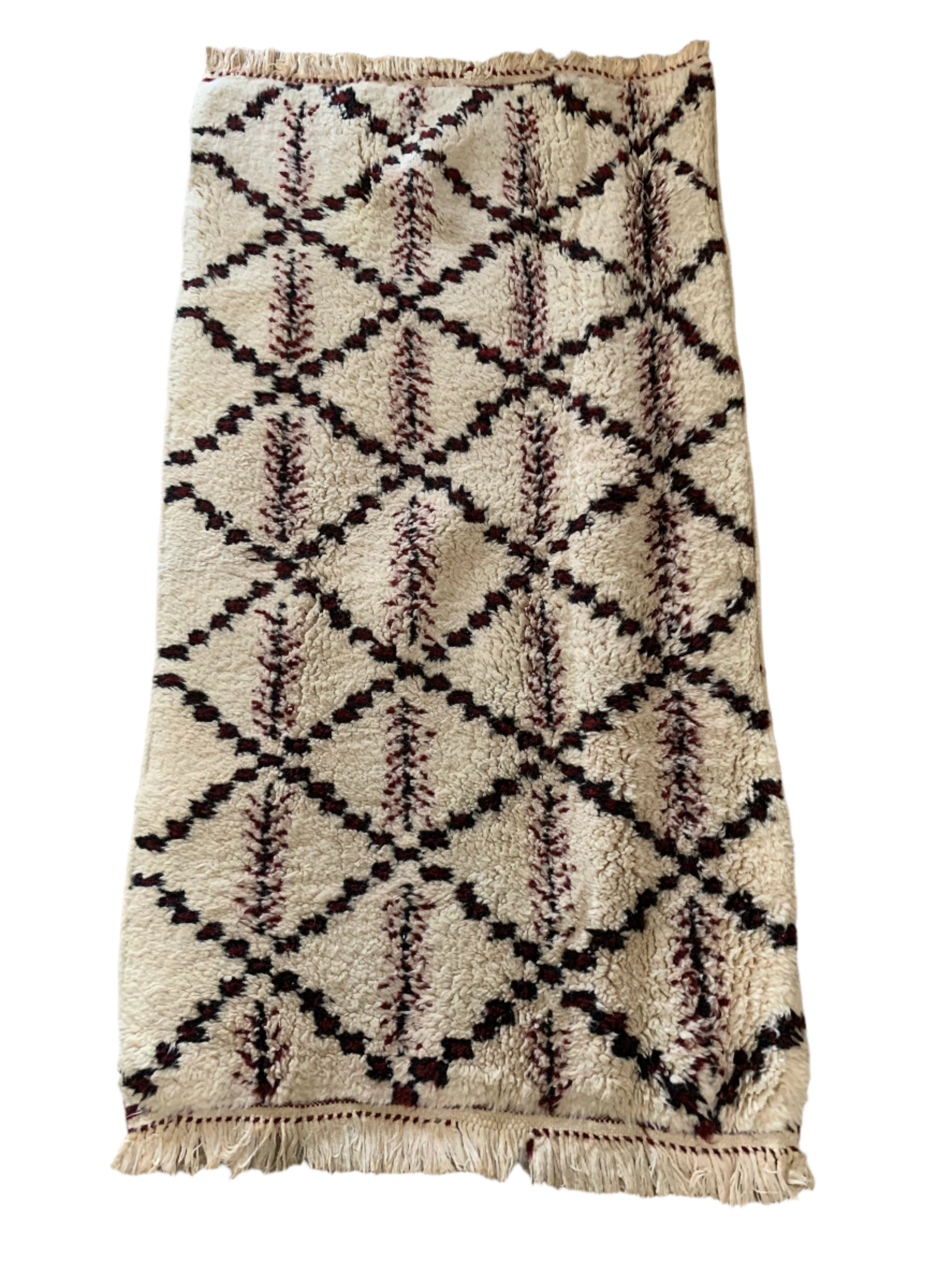 A patterned rug with a cream background showcases diamond shapes marked by black and maroon designs, resting on a stone floor.