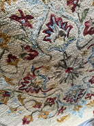 Close-up of a textured rug featuring intricate floral patterns in red, blue, yellow, and green, set against a neutral background.
