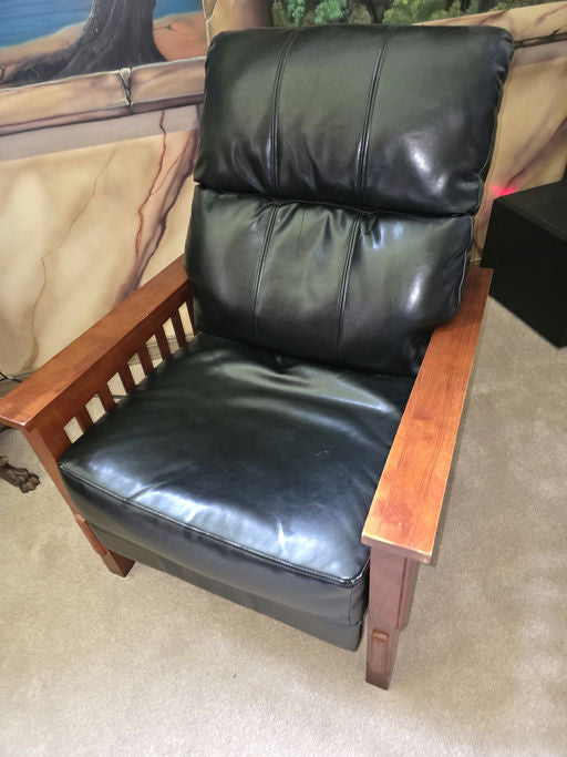 A comfortable black leather recliner with plush cushioning and wooden armrests, set against a softly colored, mural-painted wall.