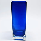 A tall, rectangular glass vase in a vibrant blue hue with a clear base, set against a white background, showcasing a sleek and modern design.