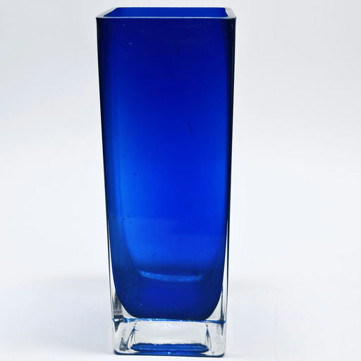 A tall, rectangular glass vase in a vibrant blue hue with a clear base, set against a white background, showcasing a sleek and modern design.