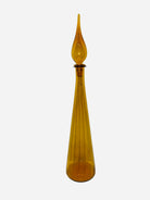 A tall, amber glass decanter with a pointed stopper, featuring vertical ridges along its body. The design is elegant and modern.
