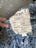 Hand holding a blue, woven carpet tag. Label states "carpet," size 5x5, material 100% cotton, made in India, dated January 12, 2021.