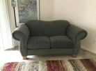 A green loveseat with plush upholstery and rolled arms sits on a light carpet. A colorful rug lies in front, and a starfish-themed artwork adorns the wall.