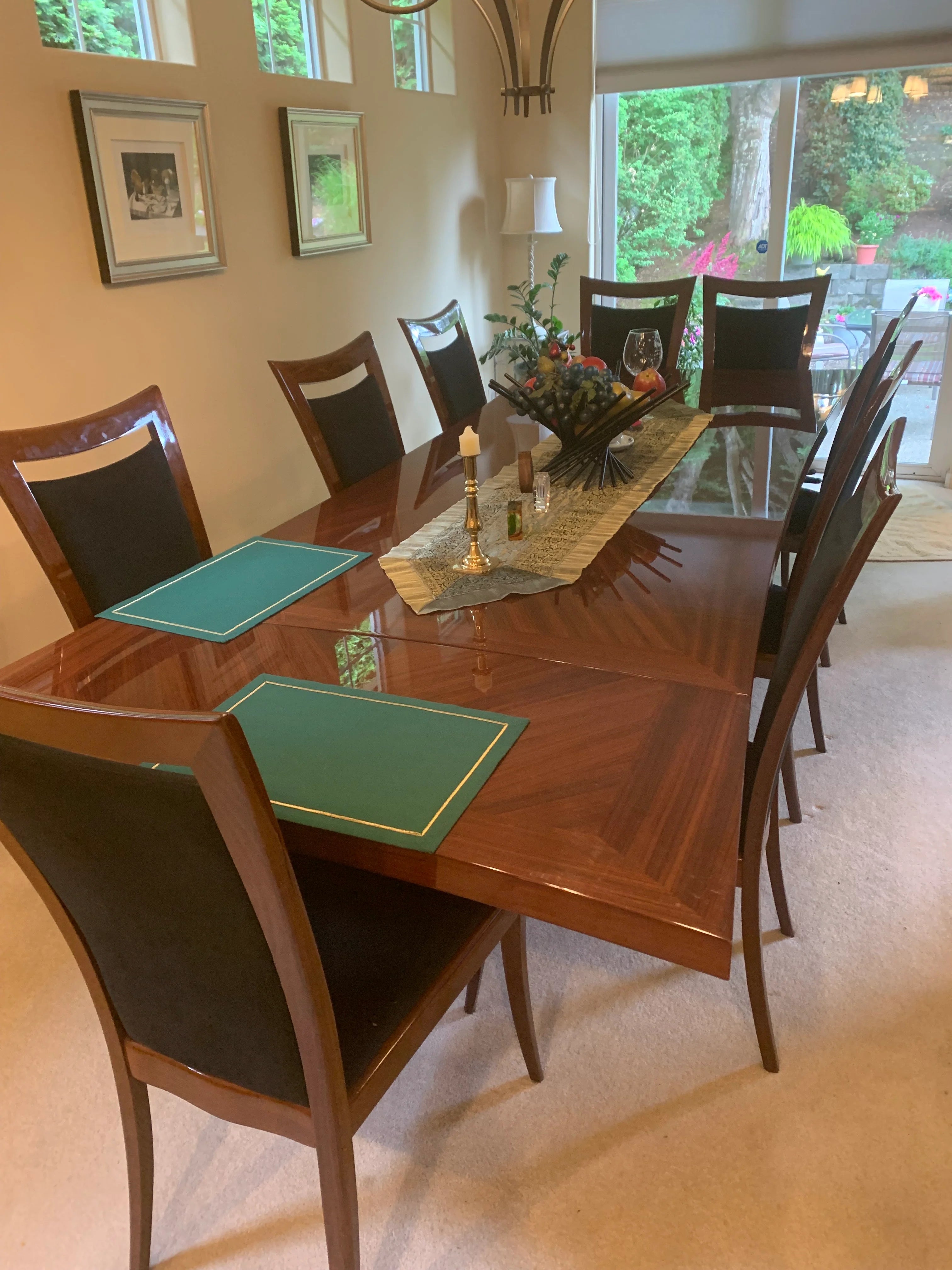 A dining room table set with eight chairs, green placemats, and a decorative centerpiece. Natural light filters through windows.