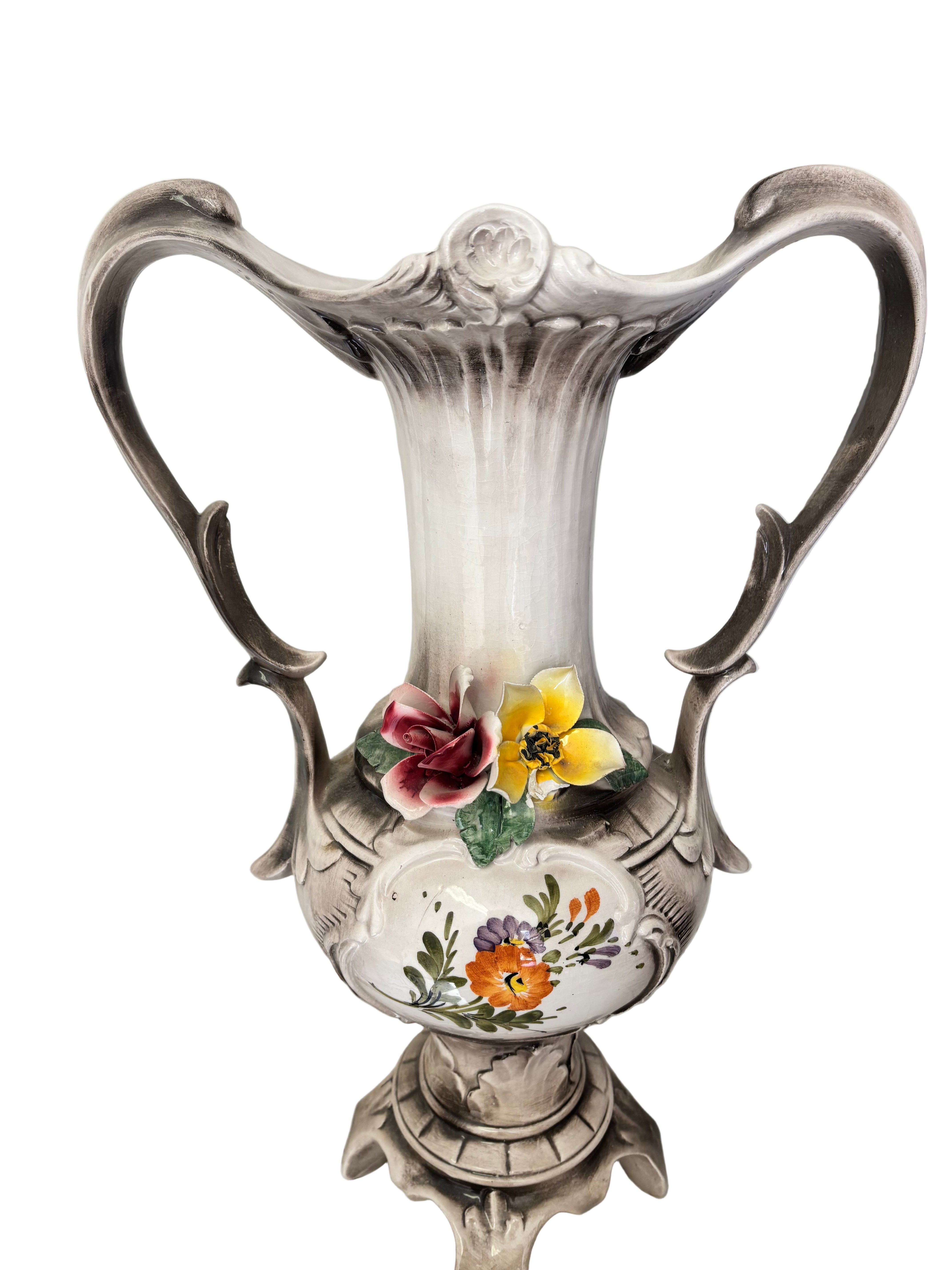 Ceramic vase with ornate design, featuring floral decorations in pink, yellow, and orange. It stands on a decorative base against a tiled surface.