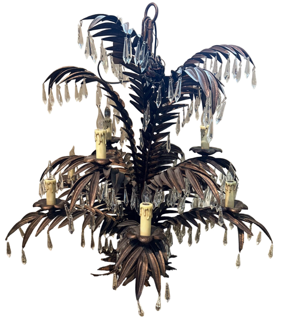A decorative chandelier resembling a palm tree, featuring metal leaves and candle holders, accented with hanging crystals, placed on a carpeted floor.
