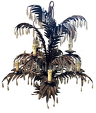 A decorative chandelier resembling a palm tree, featuring metal leaves and candle holders, accented with hanging crystals, placed on a carpeted floor.
