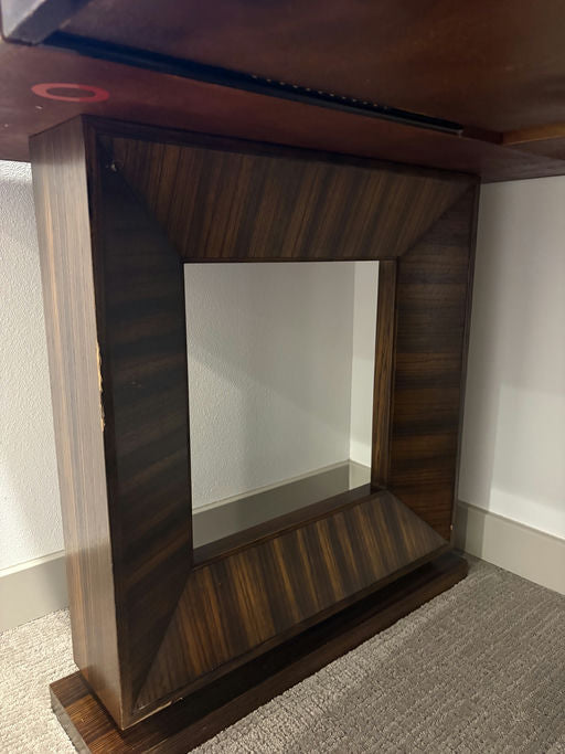 A wooden frame with a rectangular cutout sits under a table, showcasing a textured carpet and smooth wall behind it. Subtle grain patterns visible.