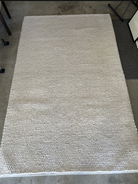 A textured, light-colored area rug with a bubble-like pattern, lying on a concrete floor, adds warmth and style to the space.