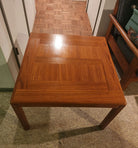 A square wooden coffee table with a glossy finish, featuring a geometric pattern on the surface, set in a room with patterned flooring.