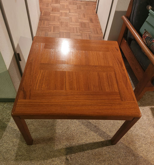 A square wooden coffee table with a glossy finish, featuring a geometric pattern on the surface, set in a room with patterned flooring.