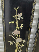 Intricate floral design on a black background, featuring soft-colored blossoms, leaves, and delicate detailing, displayed on an ornate panel.