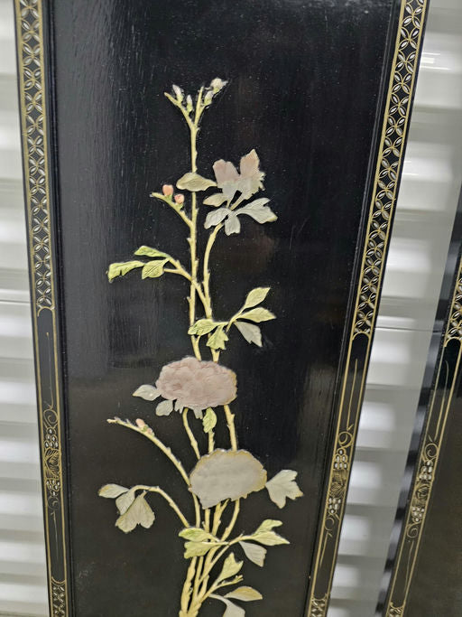 Intricate floral design on a black background, featuring soft-colored blossoms, leaves, and delicate detailing, displayed on an ornate panel.
