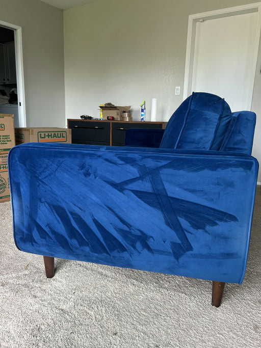 A blue couch with a textured surface has visible streaks or marks. Surrounding it are unpacked boxes and a dresser in a partially furnished room.
