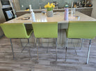 A modern kitchen scene featuring a sleek island with three green chairs, a vase of yellow tulips, and various kitchen items on the counter.