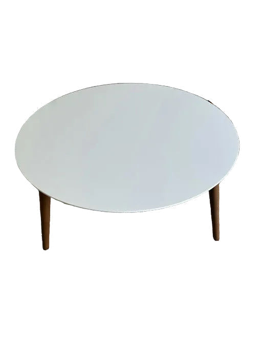 A modern round coffee table with a white top and wooden legs, placed on beige carpet, with a staircase visible in the background.