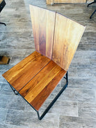 A modern wooden chair with a slatted seat and high backrest, featuring a sleek black metal frame, set against a textured tiled floor.