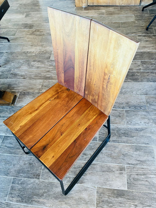 A modern wooden chair with a slatted seat and high backrest, featuring a sleek black metal frame, set against a textured tiled floor.