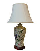 A decorative table lamp with a white lampshade and a floral ceramic base featuring a colorful bird, positioned on a wooden table.