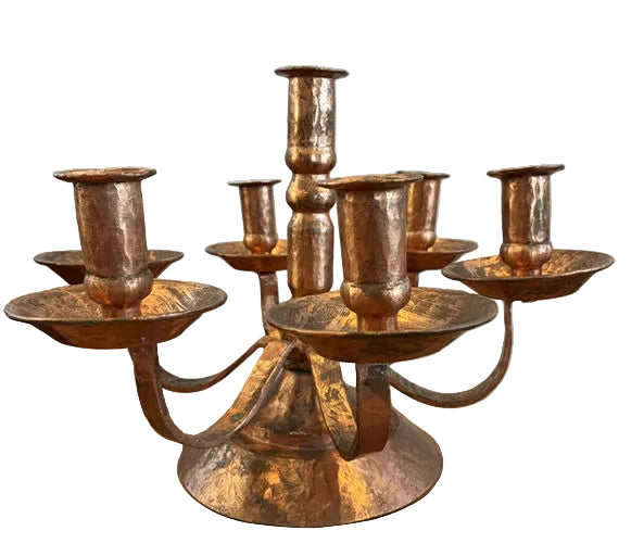A vintage copper candlestick holder with six candle holders, featuring a textured finish and a rounded base, set on a wooden surface.