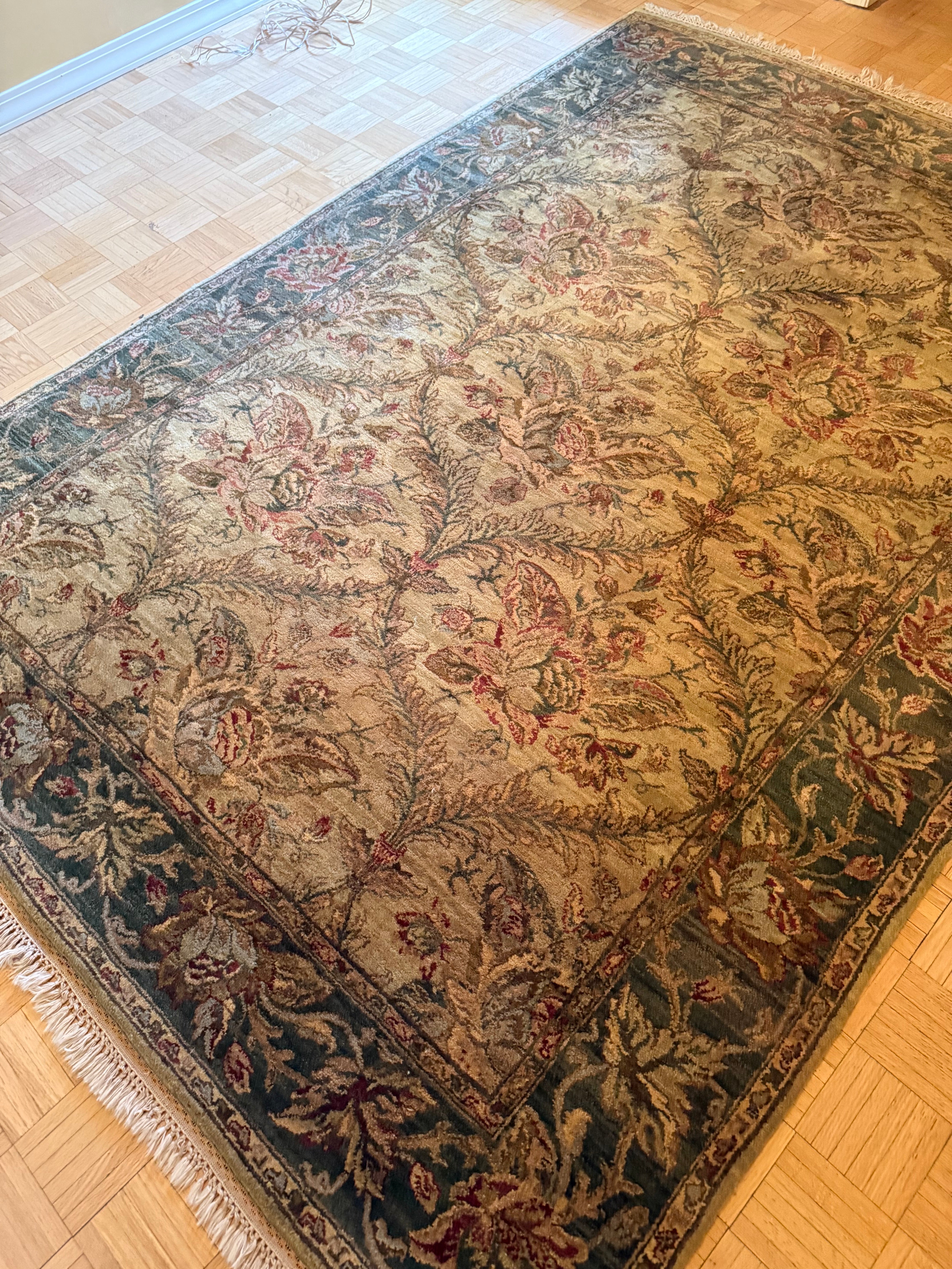 A decorative area rug featuring floral patterns in muted colors, resting on a light wood floor with a soft, textured border.