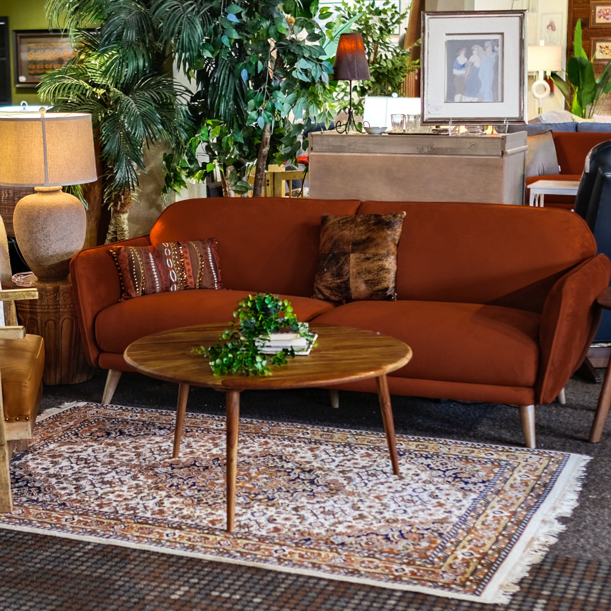 Mid-century modern rust orange sofa with accent pillows styled in Tacoma consignment furniture store, paired with round wood coffee table and traditional area rug.
