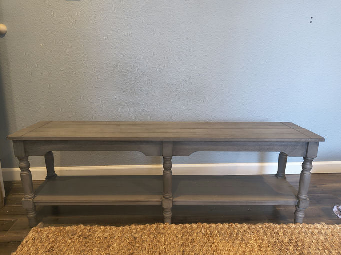 A gray wooden console table with two shelves, featuring turned legs and a smooth top, positioned against a light blue wall.