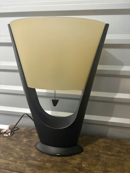 A modern black table lamp with a semi-circular frosted shade, featuring a pull chain switch and set against a textured grey background.