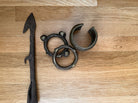 A dark metal spearhead and three circular metal rings with decorative elements, displayed on a light wooden surface.