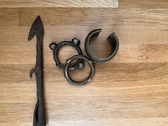 A dark metal spearhead and three circular metal rings with decorative elements, displayed on a light wooden surface.