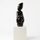Black abstract sculpture on a white pedestal against a white background