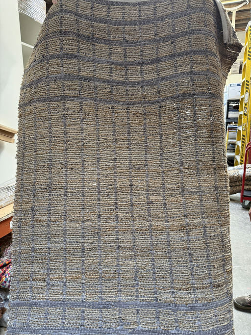 A textured woven rug displayed vertically, featuring a grid pattern in shades of brown and gray, highlighting its natural fibers and craftsmanship.