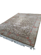 A large, ornate area rug with floral patterns in beige and orange lies on a concrete surface, partially shaded by trees in a grassy outdoor setting.