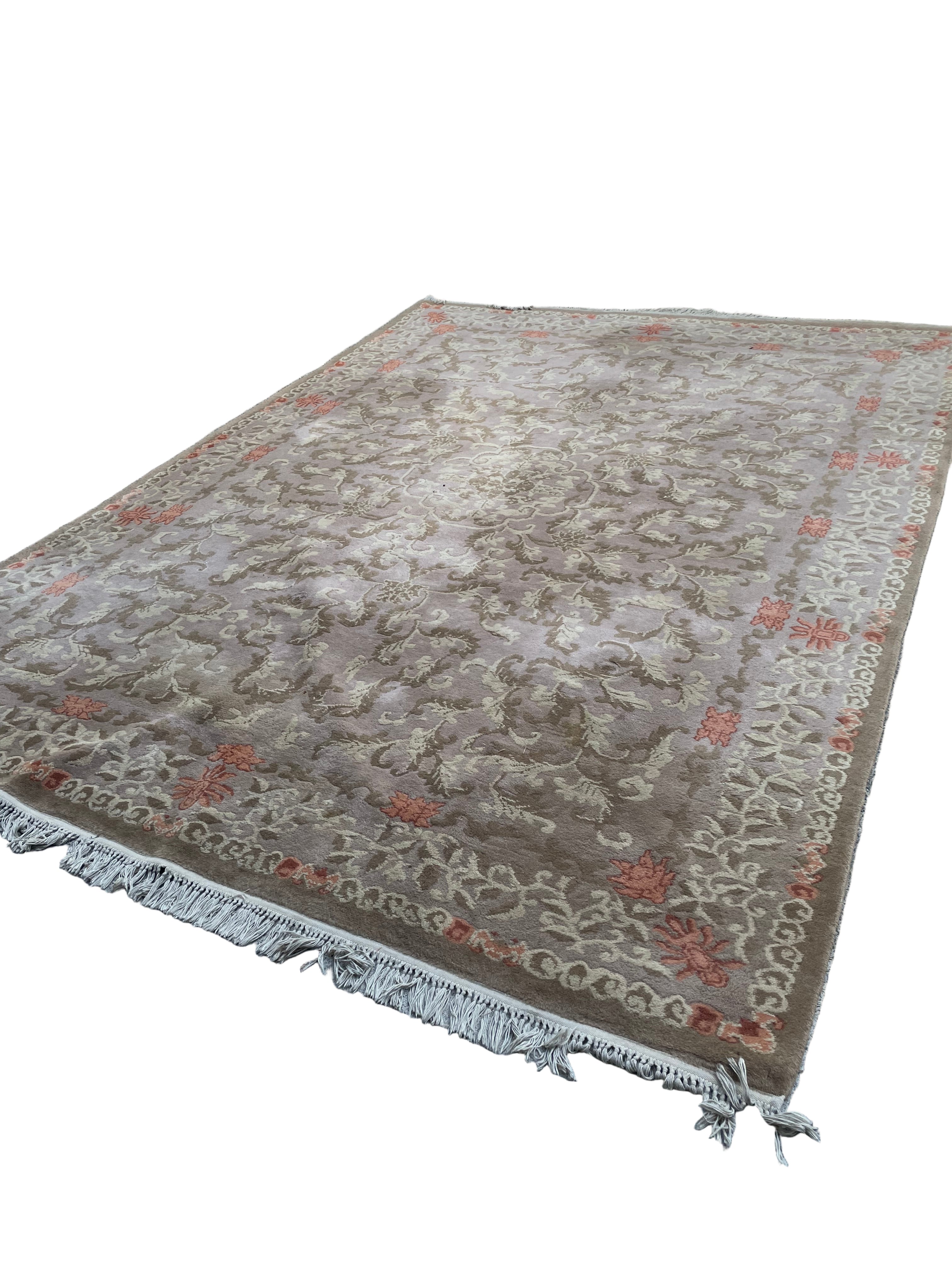 A large, ornate area rug with floral patterns in beige and orange lies on a concrete surface, partially shaded by trees in a grassy outdoor setting.