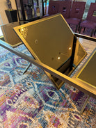 A sleek, modern coffee table with glass surfaces sits on a colorful patterned rug. Background features purple chairs and decorative items.