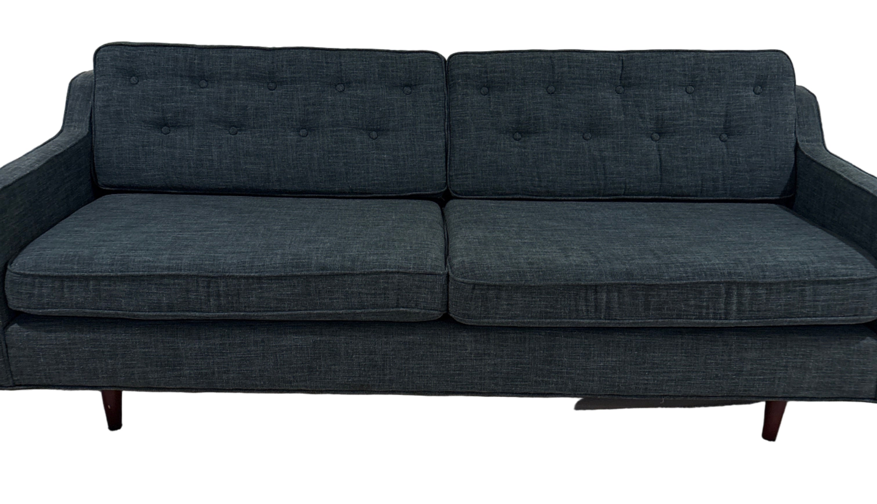 A modern, dark blue fabric sofa with button-tufted back cushions, two seats, and wooden legs, positioned on a light carpet against a plain wall.
