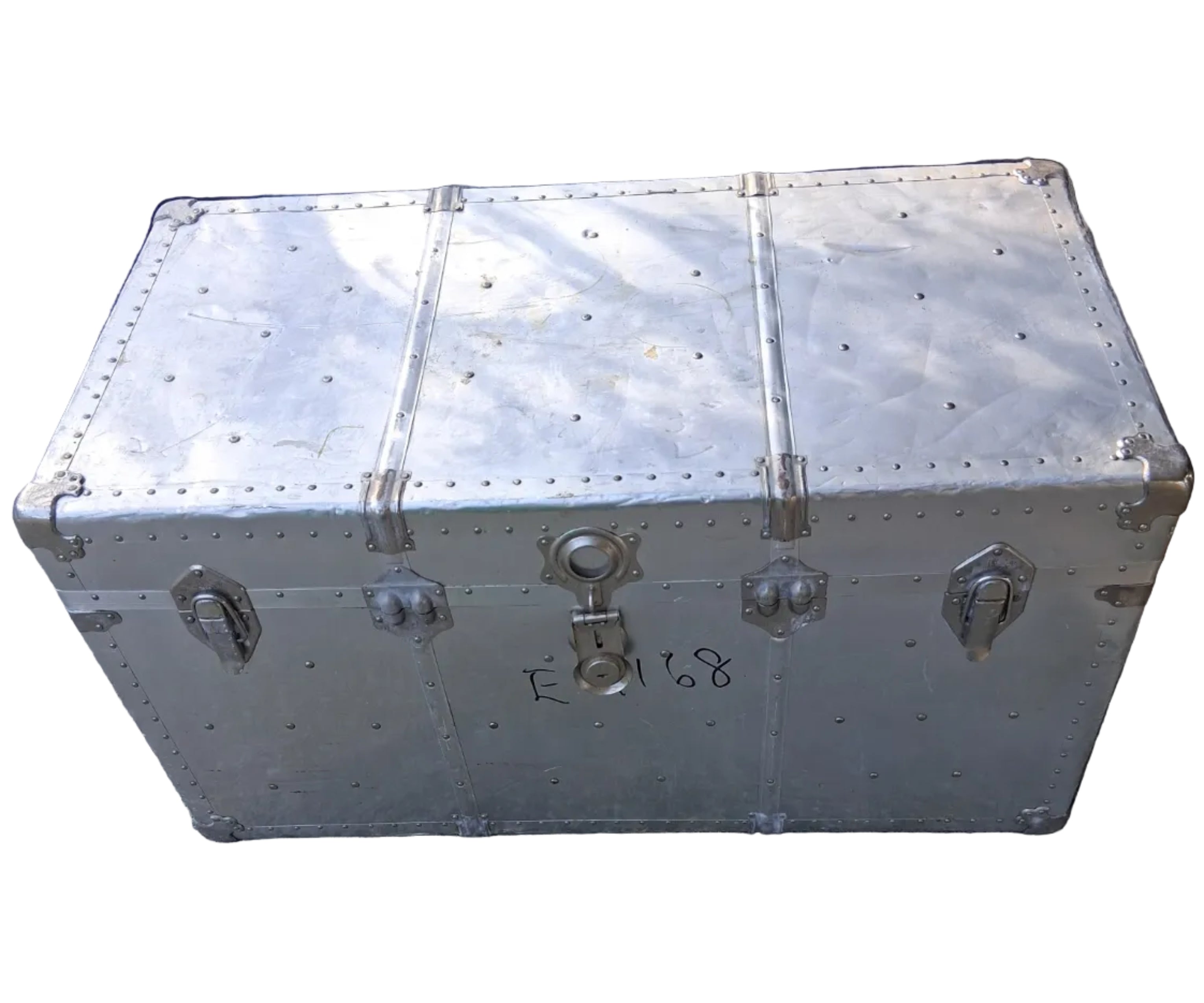 A weathered aluminum trunk with metal clasps sits on a concrete surface. Nearby, a car is partially visible, suggesting a garage setting.