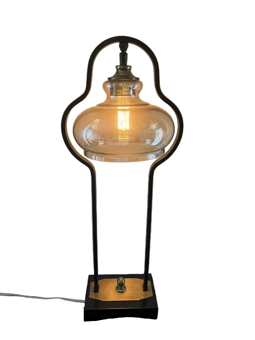 A stylish table lamp with a glass shade and a vintage bulb, set on a black base with a gold accent, providing warm, ambient light.