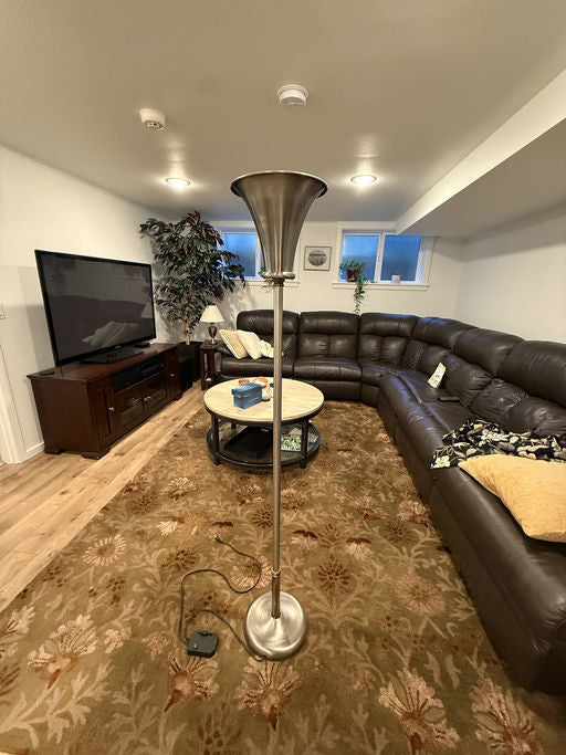 A modern living room featuring a silver floor lamp, a brown leather sectional sofa, a round coffee table, and a patterned carpet.