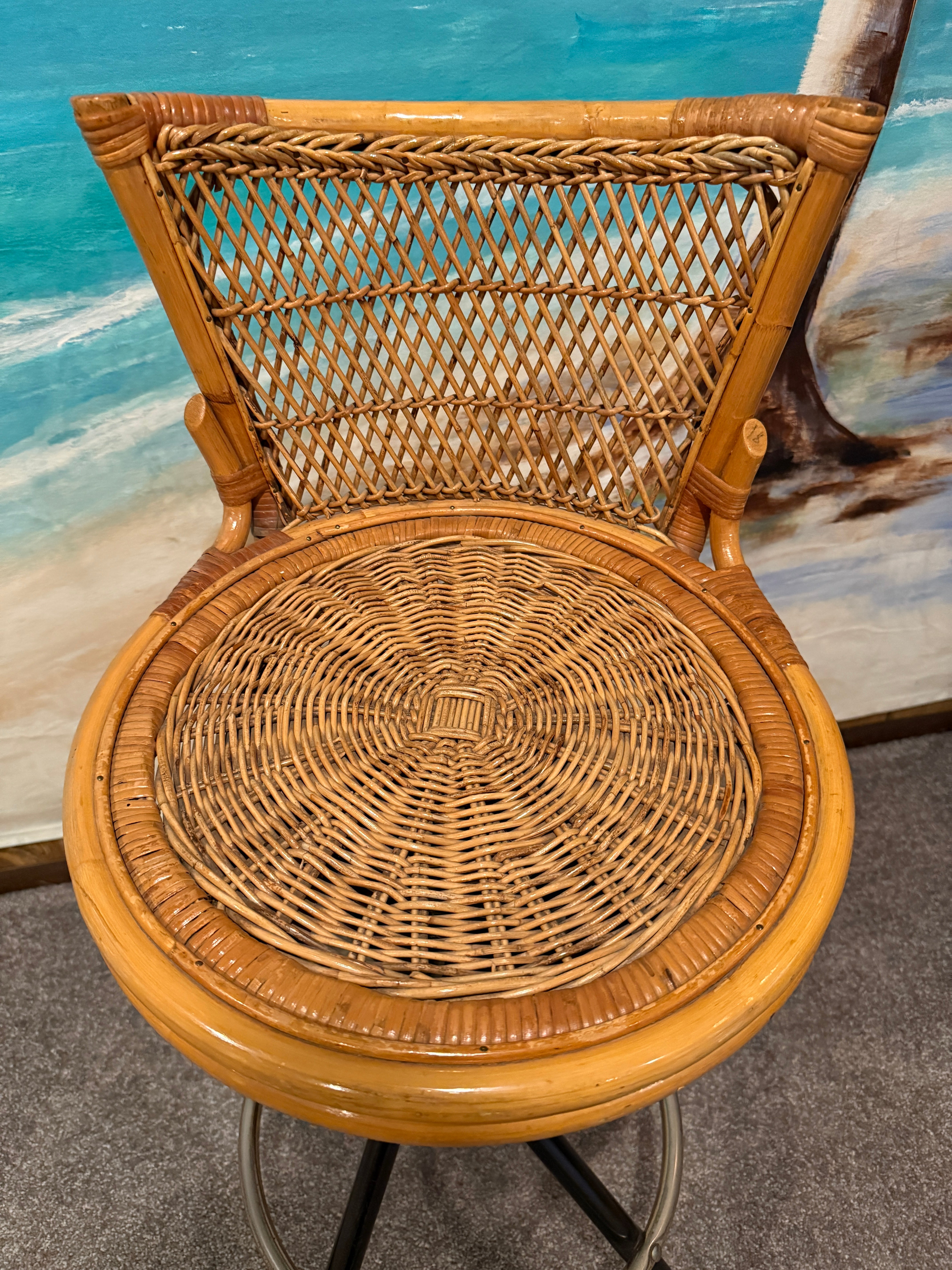 A woven rattan bar stool with a circular seat and backrest, set against a beach-themed mural featuring sandy shores and ocean colors.